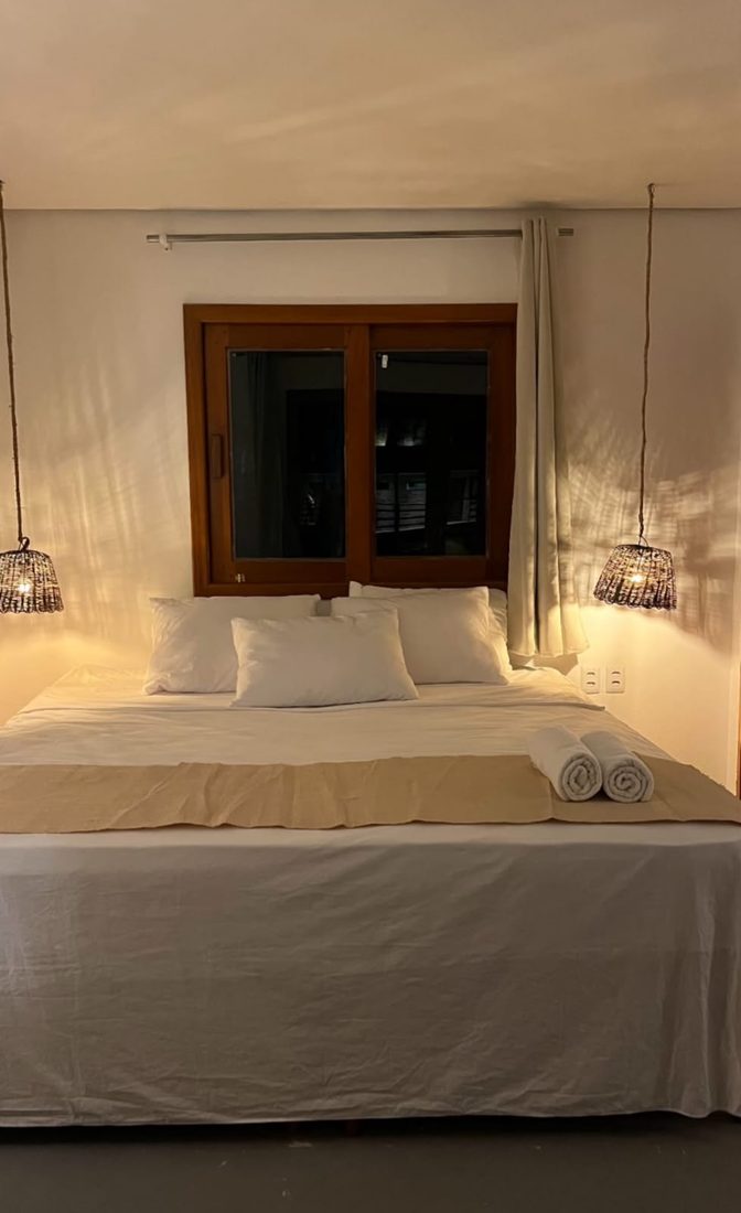 Cama de casal com luminárias de fibra dos dois lados e janela ao fundo