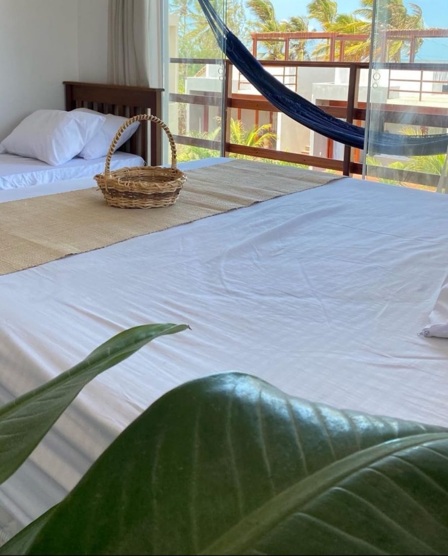 Cama com cesto de amenities e varanda com rede, vista para o mar